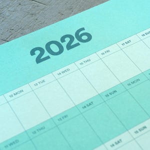 May include: A close-up of a teal 2026 calendar page. The year 2026 is printed in large, dark teal numbers at the top. The calendar grid is visible with days of the week and dates. The background is a light teal color.