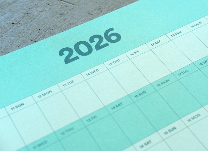 May include: A close-up of a teal 2026 calendar page. The year 2026 is printed in large, dark teal numbers at the top. The calendar grid is visible with days of the week and dates. The background is a light teal color.