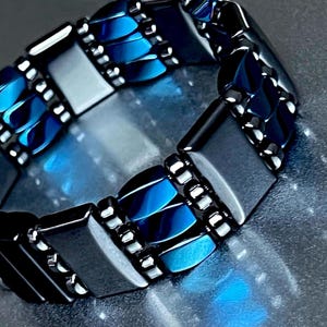 May include: A bracelet made of dark gray and blue rectangular beads. The beads are arranged in a pattern of alternating colors.