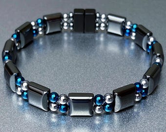 May include: A black and silver magnetic bracelet with blue beads. The bracelet is made of square-shaped hematite beads and small silver and blue beads.