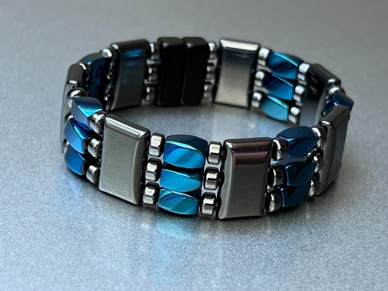 May include: A multi-layered bracelet with blue and silver magnetic beads. The bracelet is made of metal and has a modern design.