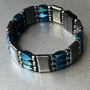 May include: A blue and silver magnetic bracelet with multiple rows of rectangular and oval-shaped beads.