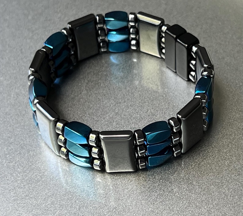 May include: A blue and silver magnetic bracelet with multiple rows of rectangular and oval-shaped beads.