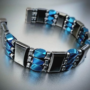May include: A silver and blue bracelet with multiple rows of beads. The beads are rectangular and oval shaped.