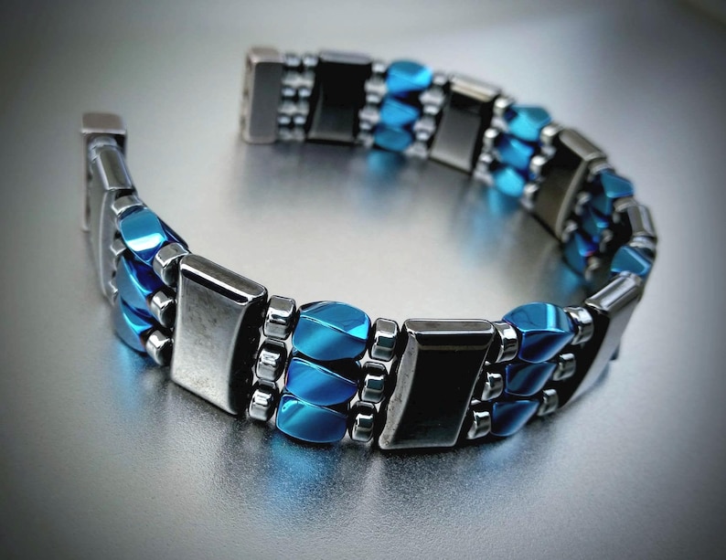 May include: A silver and blue bracelet with multiple rows of beads. The beads are rectangular and oval shaped.