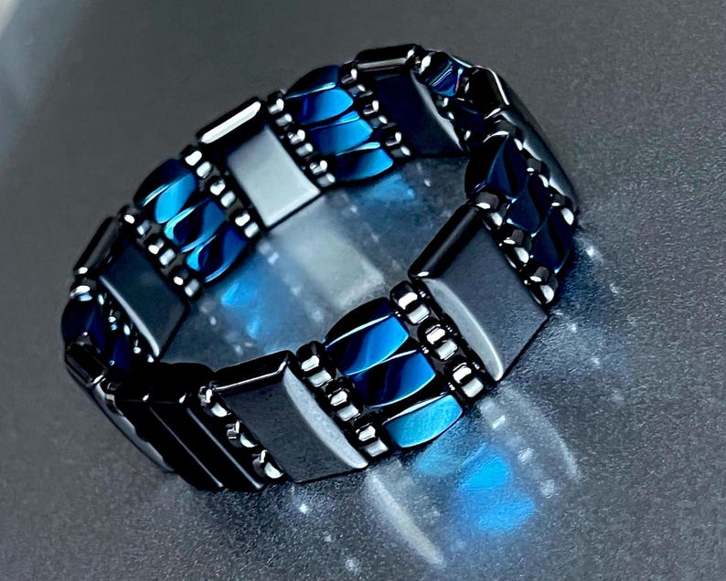 May include: A bracelet made of dark gray and blue rectangular beads. The beads are arranged in a pattern of alternating colors.