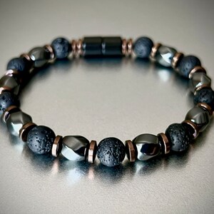 May include: A black beaded bracelet with a magnetic clasp. The bracelet features black lava rock beads, black hematite beads, and copper spacer beads.