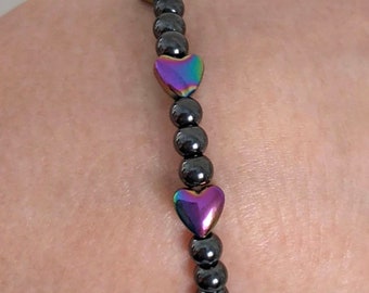 May include: A black hematite bracelet with iridescent heart-shaped charms. The bracelet is made of small round beads and has a stretchy design.