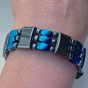 May include: A blue and silver magnetic bracelet with a clasp closure. The bracelet is made of multiple rows of beads.