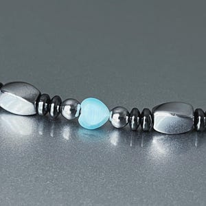 May include: A black and silver beaded bracelet with a light blue heart-shaped bead.