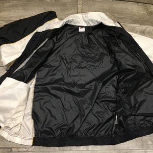 May include: Black, white, and yellow athletic jacket. The jacket is open, revealing a black interior lining and pockets. The exterior features a color block design with white and black panels, and yellow accents.
