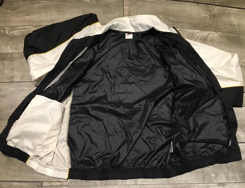 May include: Black, white, and yellow athletic jacket. The jacket is open, revealing a black interior lining and pockets. The exterior features a color block design with white and black panels, and yellow accents.