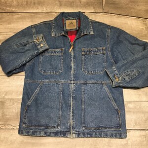 May include: A blue denim jacket featuring a full-length front zipper, a pointed collar, and long sleeves with buttoned cuffs. The jacket includes two chest pockets with flaps and two large lower pockets, with a red plaid lining visible at the collar.