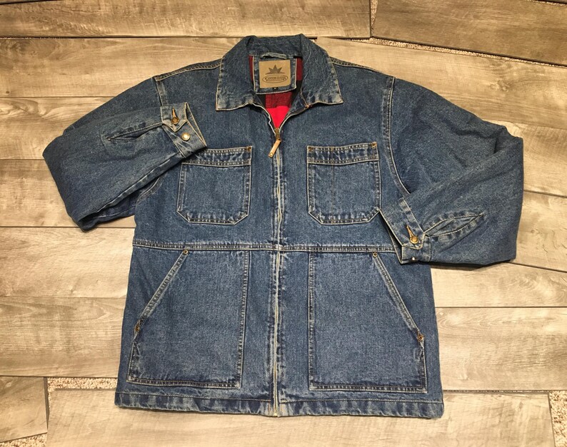 May include: A blue denim jacket featuring a full-length front zipper, a pointed collar, and long sleeves with buttoned cuffs. The jacket includes two chest pockets with flaps and two large lower pockets, with a red plaid lining visible at the collar.