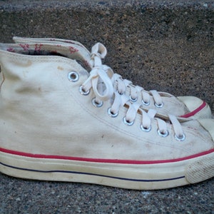 Pode incluir: T&ecirc;nis branco de lona de cano alto com acabamento vermelho ao redor da sola e cadar&ccedil;os brancos.