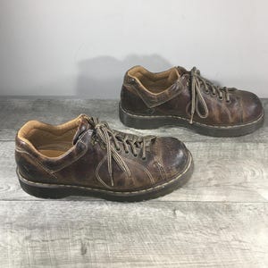 Puede incluir: Un par de zapatos de cuero marrón con cordones. Los zapatos tienen un aspecto desgastado y envejecido, con arrugas visibles y variaciones de color. Las suelas son de color marrón oscuro y el interior está forrado con un material marrón más claro. Zapatos informales.