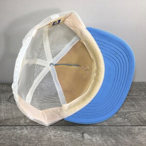 May include: A blue and white mesh trucker hat with a white mesh back and a blue front. The hat has a white adjustable strap in the back.