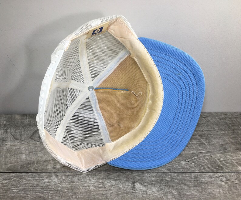 May include: A blue and white mesh trucker hat with a white mesh back and a blue front. The hat has a white adjustable strap in the back.