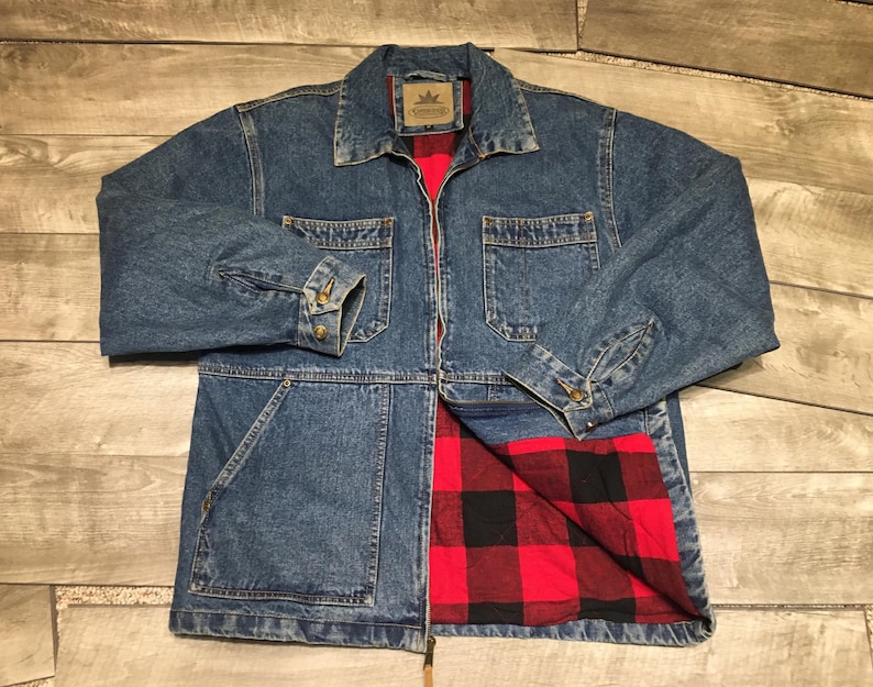 May include: A blue denim jacket featuring a classic collar, a full-length front zipper, and two chest pockets. The interior is lined with a red and black buffalo plaid pattern. The sleeves have buttoned cuffs, and the jacket has a visible brand label.