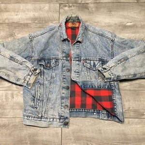 May include: A light blue denim jacket with a red and black plaid flannel lining. The jacket has a button closure and two front pockets.