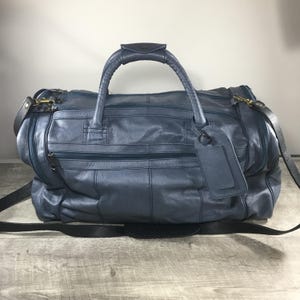 May include: A blue leather duffel bag with a top handle and a detachable shoulder strap. The bag has a rectangular shape with multiple zippered compartments and a luggage tag. The bag is approximately 51 cm long.