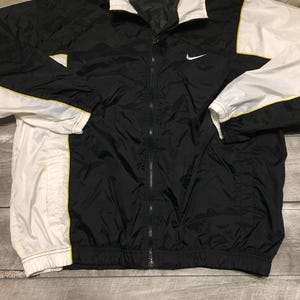May include: Black and white Nike windbreaker jacket with a full zipper. The jacket features white sleeves with yellow trim and a white collar. A small Nike swoosh logo is on the chest.