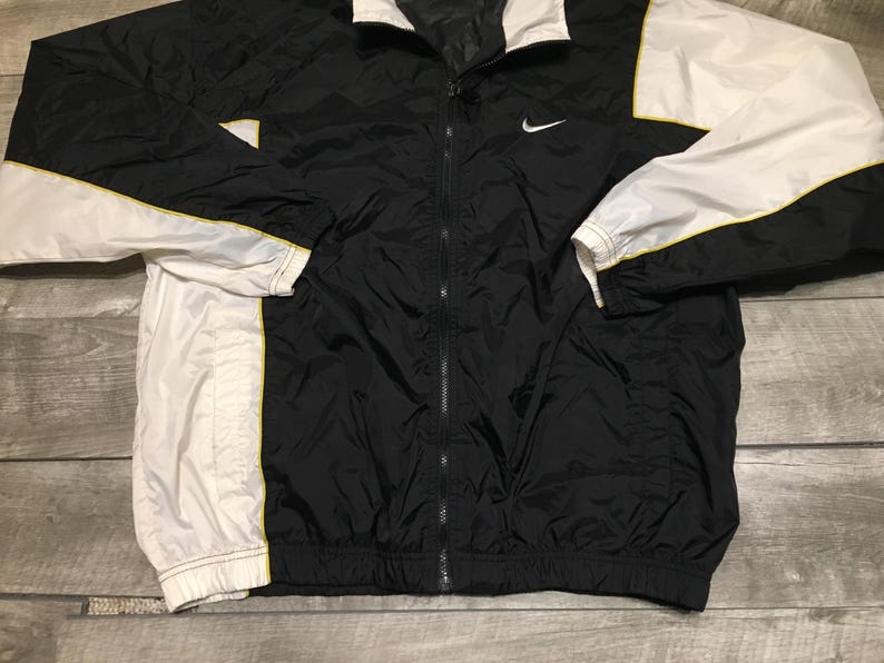 May include: Black and white Nike windbreaker jacket with a full zipper. The jacket features white sleeves with yellow trim and a white collar. A small Nike swoosh logo is on the chest.