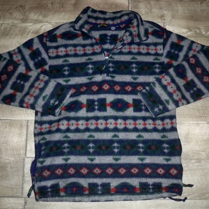 May include: A gray fleece pullover with a blue, green, and red geometric pattern. The pullover has a quarter-zip closure and a drawstring at the bottom.
