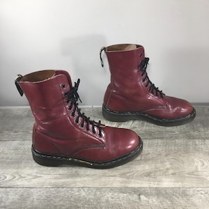 May include: A pair of burgundy leather boots with black laces. The boots have a classic design with a mid-calf height and a sturdy sole. The boots are approximately 10 inches tall.