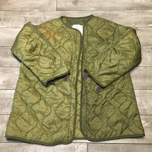 K&ouml;nnte beinhalten: Eine gr&uuml;ne gesteppte Jacke mit Druckknopfverschluss. Die Jacke hat ein Rautenmuster und ist aus leichtem Material gefertigt.