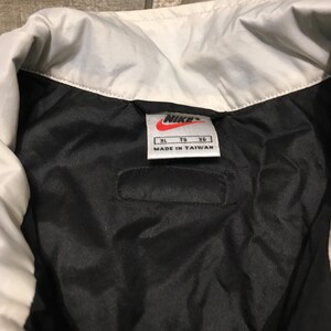 May include: Close-up of a black and white Nike jacket interior. The jacket has a white collar and a black interior. A tag with the Nike logo and "Made in Taiwan" is visible.