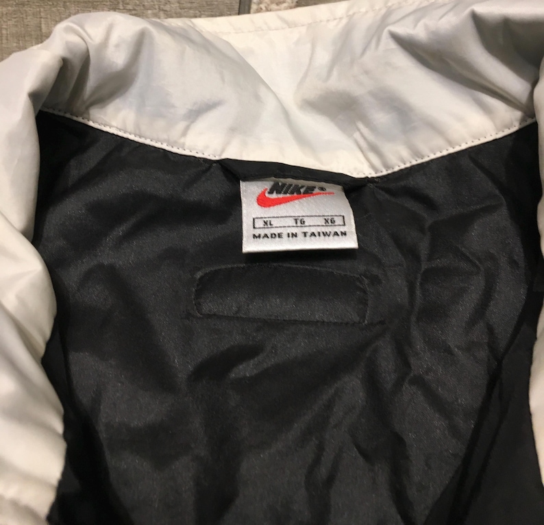 May include: Close-up of a black and white Nike jacket interior. The jacket has a white collar and a black interior. A tag with the Nike logo and "Made in Taiwan" is visible.
