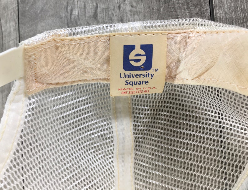May include: White mesh baseball cap with a brown adjustable strap and a white label that says "University Square" in blue lettering. The label also says "Made in USA" and "One Size Fits All".