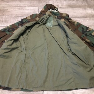K&ouml;nnte beinhalten: Eine gr&uuml;ne, braune und schwarze Tarnjacke mit Kapuze. Die Jacke ist ge&ouml;ffnet und auf links gedreht, wodurch ein gr&uuml;nes Futter sichtbar wird.