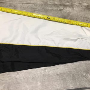May include: A black and white jacket sleeve with a yellow accent. A yellow measuring tape is laid across the sleeve, showing measurements in inches. The jacket has a white upper section and a black lower section.