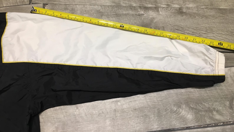May include: A black and white jacket sleeve with a yellow accent. A yellow measuring tape is laid across the sleeve, showing measurements in inches. The jacket has a white upper section and a black lower section.