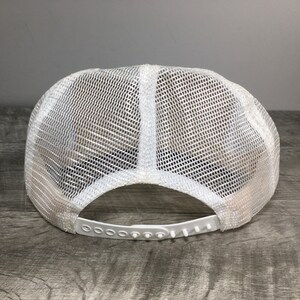 May include: White mesh trucker hat with a white plastic adjustable strap. The hat is made of a breathable mesh material and has a classic trucker hat style.