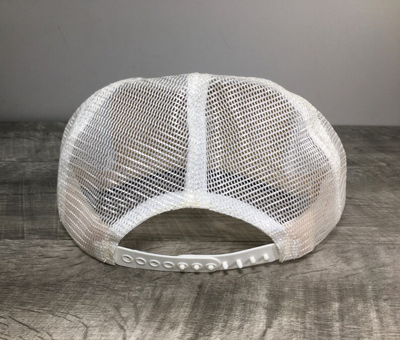 May include: White mesh trucker hat with a white plastic adjustable strap. The hat is made of a breathable mesh material and has a classic trucker hat style.