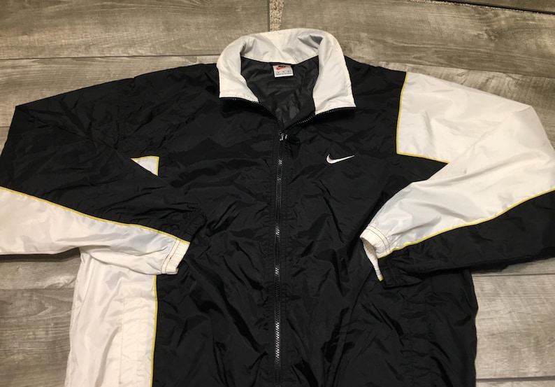 May include: Black and white Nike windbreaker jacket with a full zipper closure. The jacket features a white collar, white sleeves, and yellow trim. A white Nike swoosh logo is on the left chest.