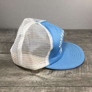 May include: A light blue and white mesh trucker hat with the text "The North Face" embroidered in white on the front.