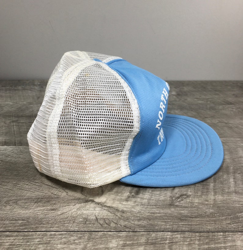 May include: A light blue and white mesh trucker hat with the text "The North Face" embroidered in white on the front.