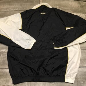 May include: Black and white Nike windbreaker jacket with yellow trim. The jacket has a white collar and sleeves, with a black body. The Nike logo is visible on the back of the collar. The jacket is made of a lightweight material.