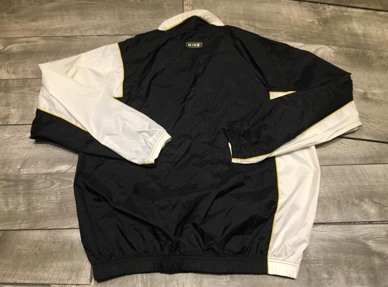 May include: Black and white Nike windbreaker jacket with yellow trim. The jacket has a white collar and sleeves, with a black body. The Nike logo is visible on the back of the collar. The jacket is made of a lightweight material.