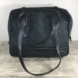 Op de afbeelding: Een zwarte leren en nylon tote bag met een enkele bovenste handgreep en een lange schouderriem.