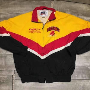 May include: Yellow, red, black, and white racing jacket with the text "Kodak Film Racing" and "Marlin 4". The jacket has a full zipper, a red collar, and black sleeves. The jacket is made of a lightweight material.
