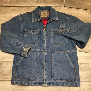 May include: A blue denim jacket featuring a full-length front zipper, a pointed collar, and long sleeves with buttoned cuffs. The jacket includes two chest pockets with flaps and two large lower pockets. A red lining is visible inside the collar.