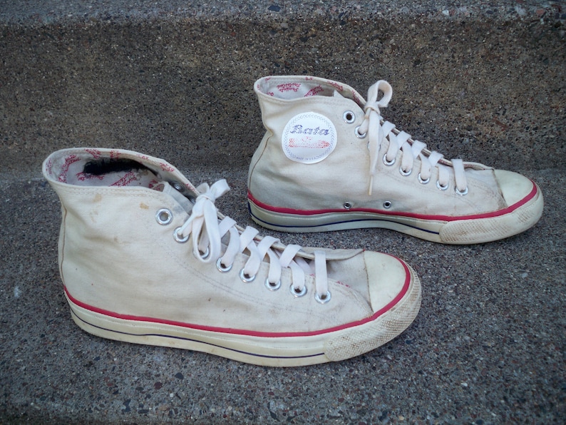 Pode incluir: Um par de t&ecirc;nis branco de lona de cano alto com detalhes vermelhos e cadar&ccedil;os brancos. Os t&ecirc;nis t&ecirc;m uma etiqueta da marca Bata no lado.