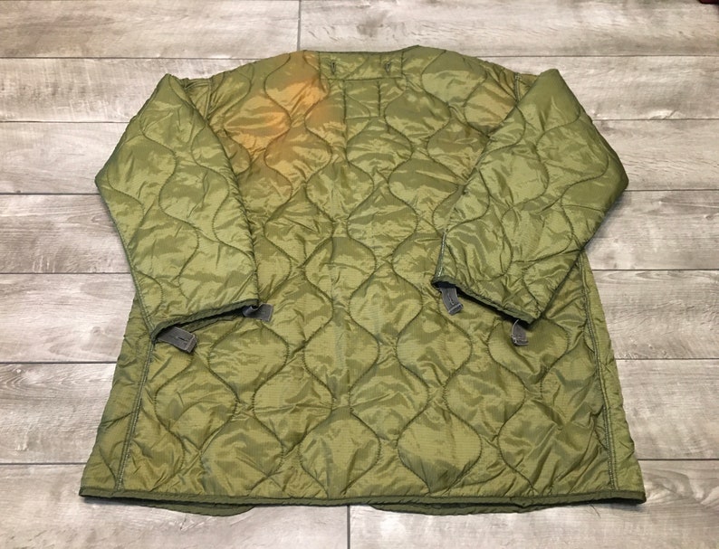 K&ouml;nnte beinhalten: Eine gr&uuml;ne gesteppte Jacke mit Rei&szlig;verschluss und Druckkn&ouml;pfen. Die Jacke hat ein rautenf&ouml;rmiges Steppmuster und ist aus leichtem Material gefertigt.