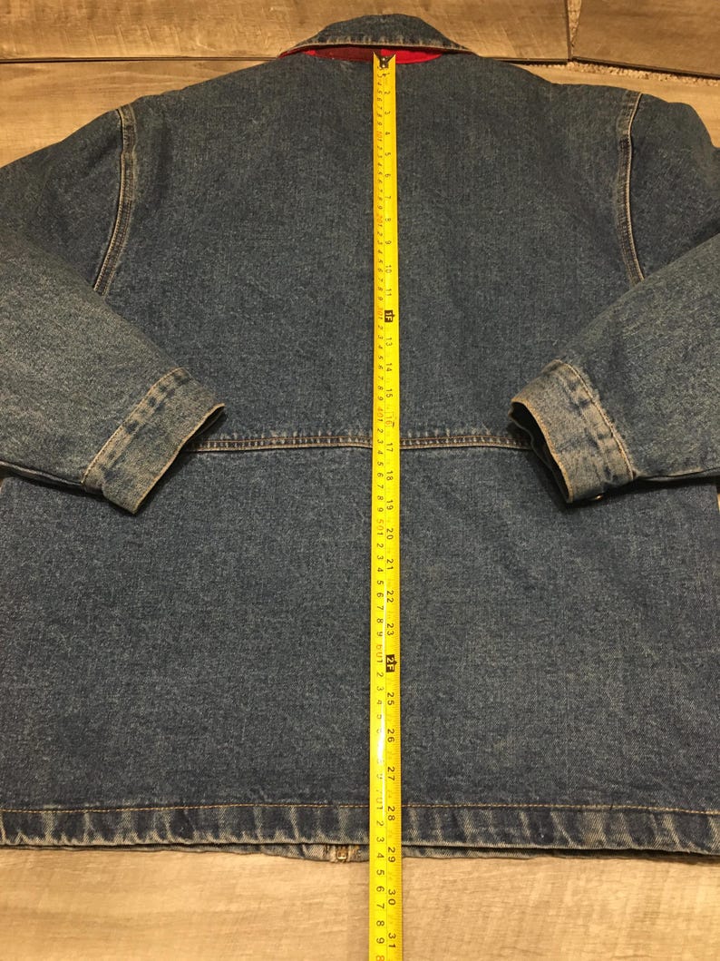 May include: A blue denim jacket with a red collar lining, featuring a yellow measuring tape placed vertically down the center back, showing a total length of approximately 31 inches from the collar seam to the bottom hem of the garment.