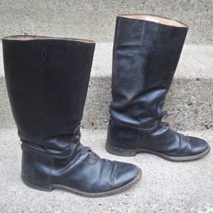 Puede incluir: Un par de botas de montar de cuero negro con cordones. Las botas son altas y tienen una punta puntiaguda.